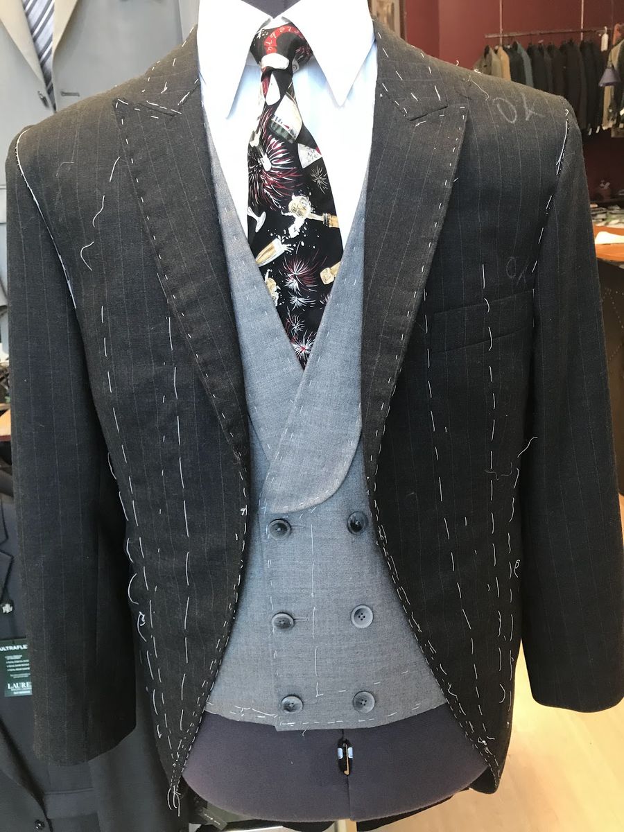A charcoal windowpane jacket and a gray double-breasted vest on a dress form, both hand-basted with white thread for a fitting