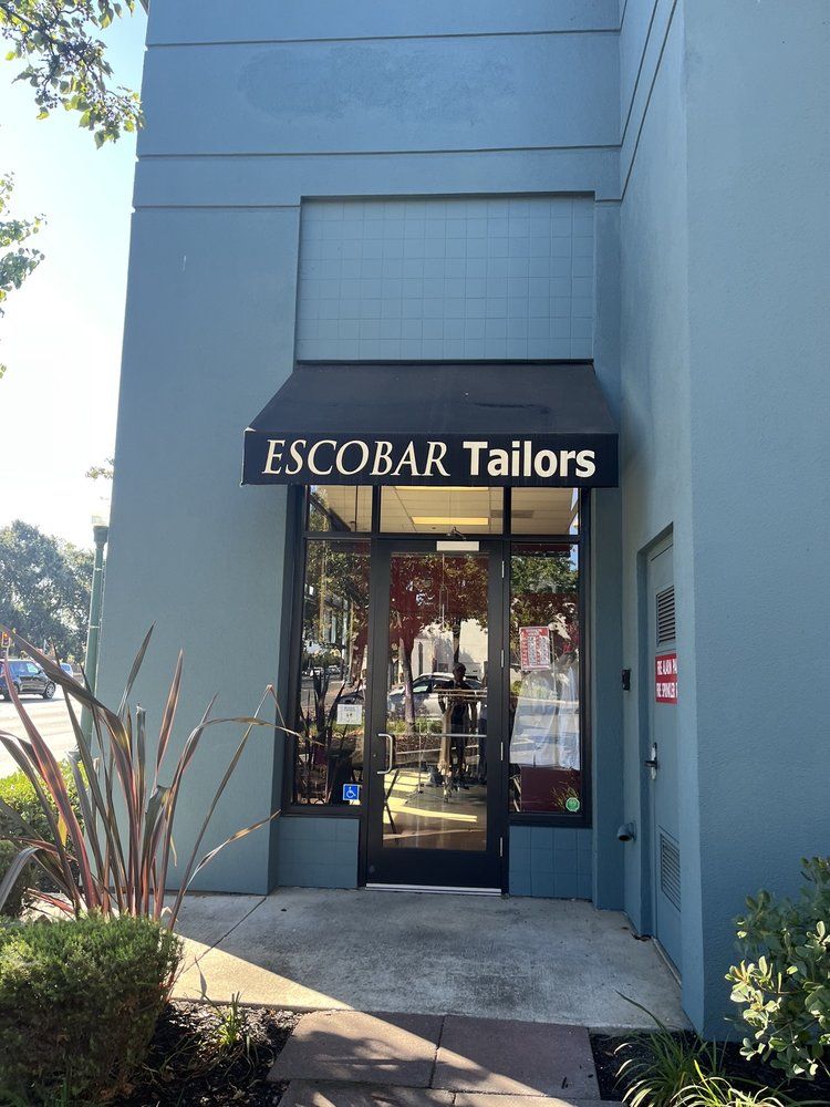 The glass entrance door beneath a black awning reading Escobar Tailors, on a blue-gray building