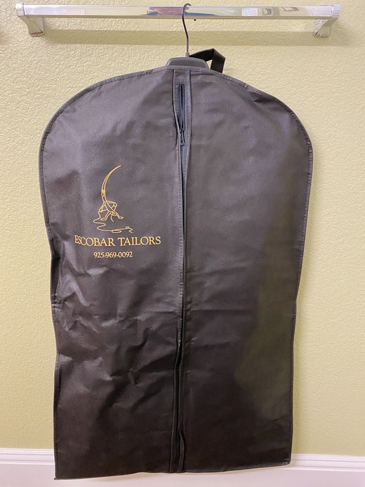 A navy Escobar Tailors garment bag with the gold needle-and-thread logo and the shop's phone number
