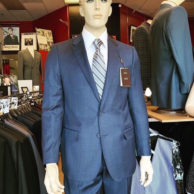 A mannequin in a blue suit, striped tie and white shirt in the showroom, with racks and framed photos behind it