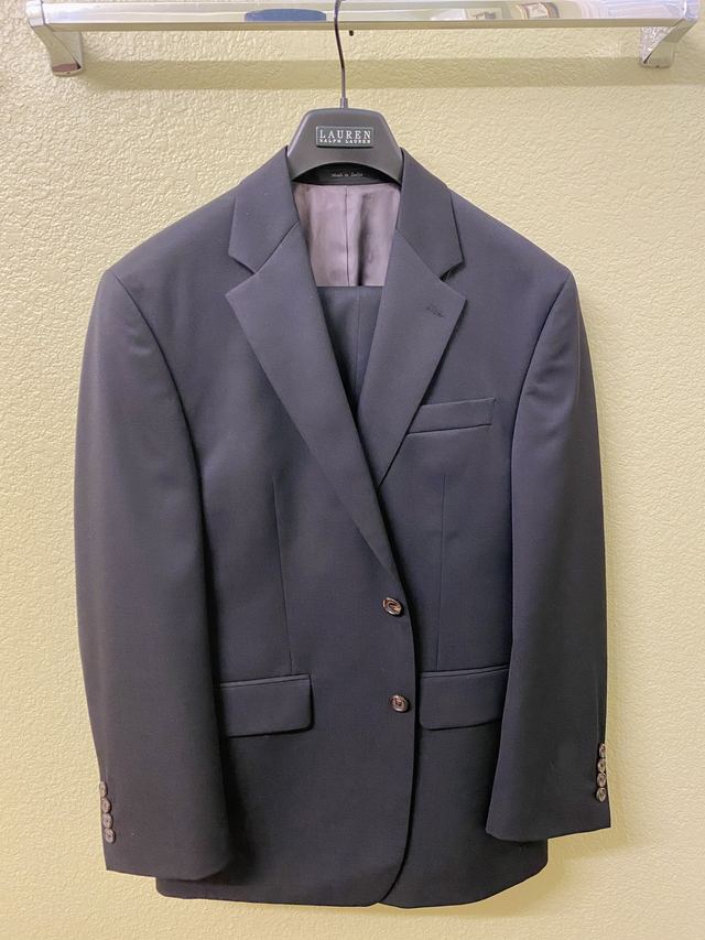A navy two-button suit jacket and trousers on a wooden hanger against a cream wall