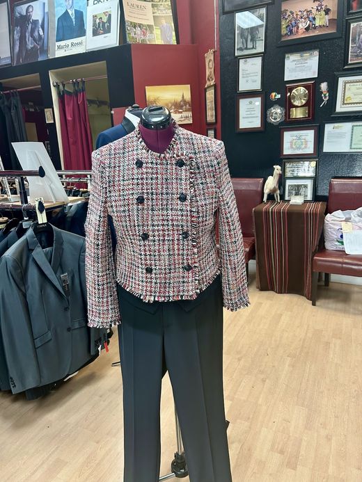 A double-breasted pink, white and black tweed women's jacket over dark trousers on a dress form
