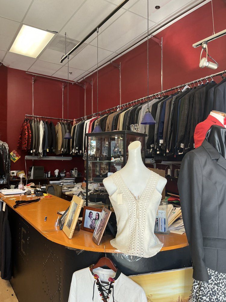 A curved wooden counter with a lace top on a dress form, in front of racks of suits along red walls